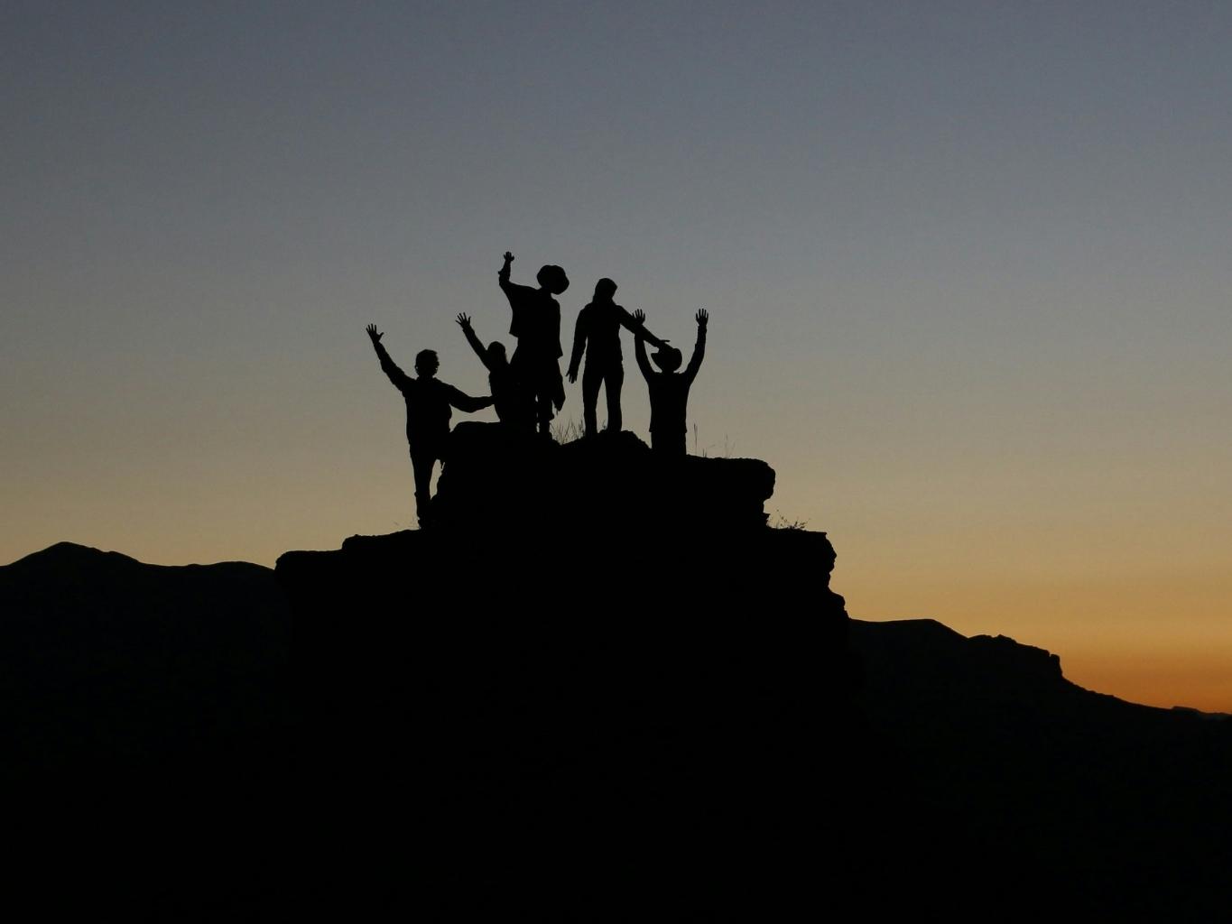 Grupo de personas celebrando en la cima de una montaña al atardecer, simbolizando logro y trabajo en equipo