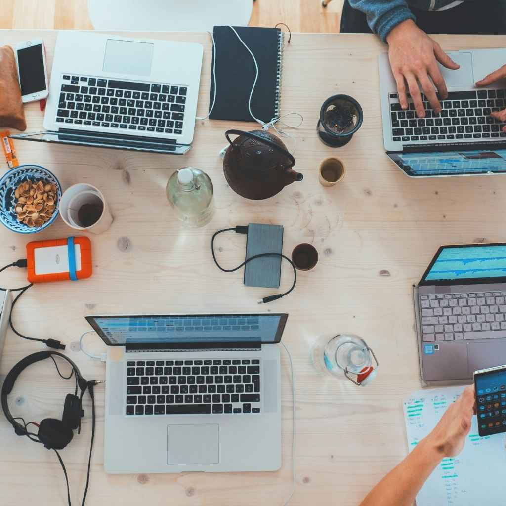 Vista cenital de una mesa de trabajo con ordenadores portátiles, dispositivos y manos trabajando en equipo