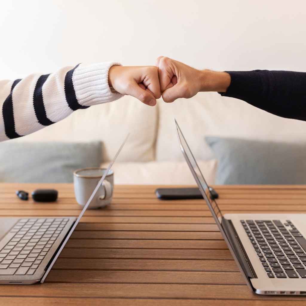 Dos personas chocando los puños entre portátiles, simbolizando colaboración digital y confianza profesional