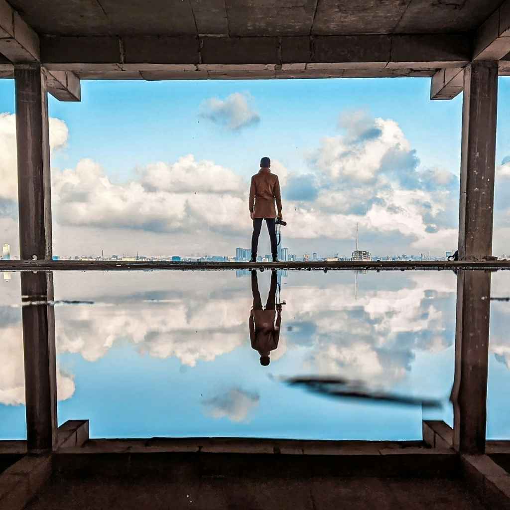 Persona contemplando el horizonte urbano desde un edificio en construcción, reflejada en el agua